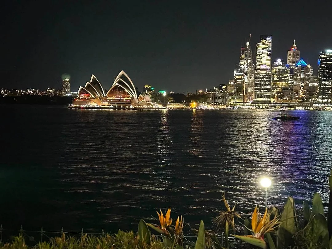 Sydney Opera House and the city skyline lit up at night, seen across the harbour