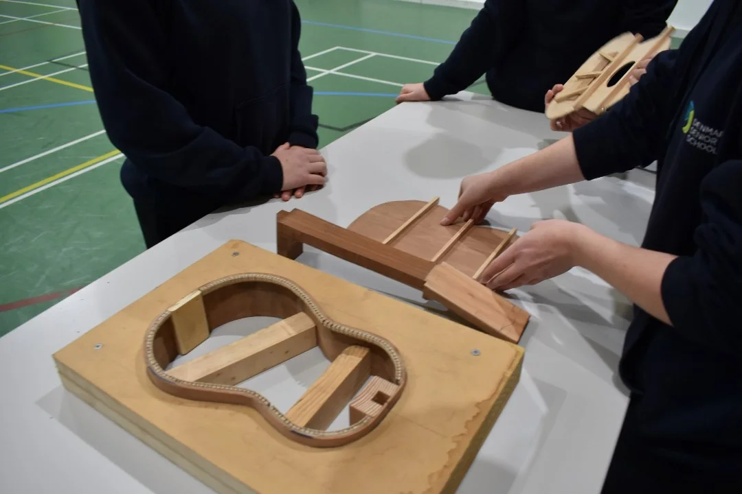 Students shaping the wooden body of a handmade guitar